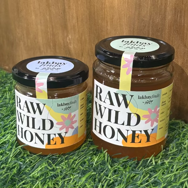 Two jars of Lakbay Finds raw wild honey, light amber, resting on grass